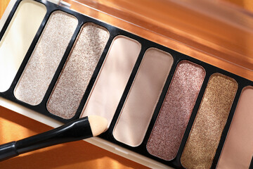Colorful eyeshadow palette and makeup applicator on orange background with shadows, flat lay