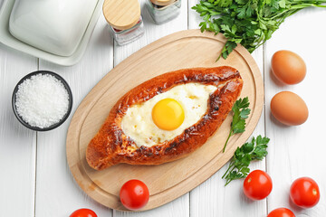 Tasty khachapuri with cheese, eggs and other products on white wooden table, flat lay