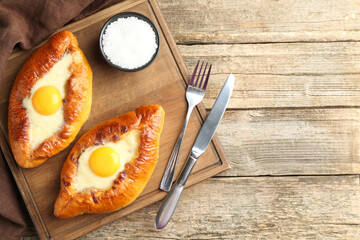 Tasty khachapuris with cheese and eggs served on wooden table, flat lay. Space for text