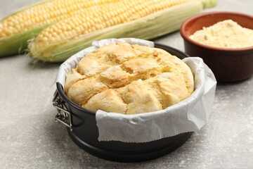 Freshly baked cornbread in cake pan on grey textured table, closeup