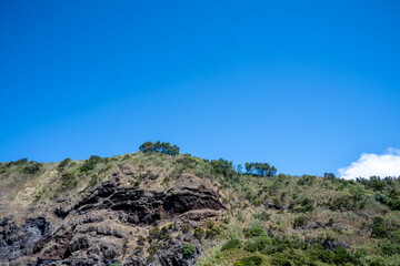 Rugged coastal cliff located on the volcanic island of Sao Miguel in the Azores, under a clear blue sky with lush vegetation