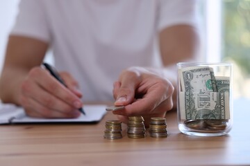 Glass jar with money and man budgeting at wooden desk, selective focus
