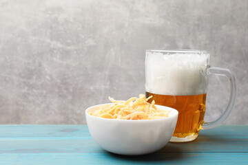 Dried squid shavings and glass mug of beer on light blue wooden table against grey background, closeup. Space for text