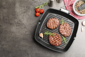 Pan with grilled patties, tomatoes and spices on grey table, flat lay. Space for text