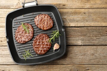 Pan with grilled patties and spices on wooden table, top view. Space for text