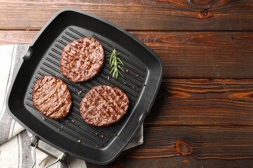 Pan with grilled patties and spices on wooden table, top view. Space for text