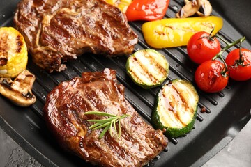 Pan with grilled beef steaks, rosemary and vegetables on grey textured table, above view