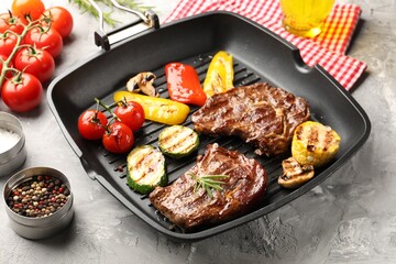 Pan with grilled beef steaks, mushrooms, vegetables and spices on grey textured table, closeup