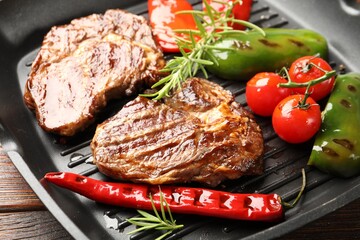 Pan with grilled beef steaks, rosemary and vegetables on wooden table, closeup