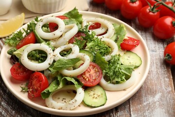 Delicious salad with squid rings, vegetables and spices on wooden table, closeup