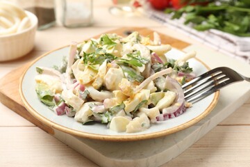 Tasty salad with squid rings, onion and eggs served on light wooden table, closeup