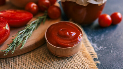 Ketchup in a wooden bowl with fresh tomatoes and rosemary.