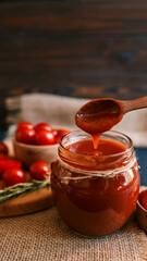 Tomato sauce dripping from a wooden spoon into a jar.