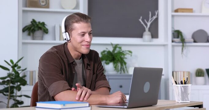 Man in headphones passing online test via laptop at table indoors