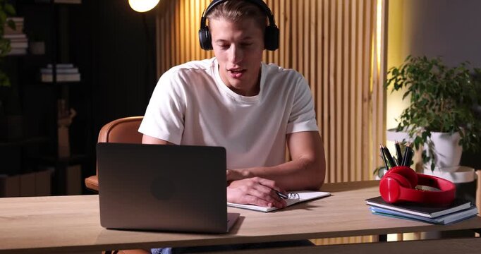 Man in headphones passing online test via laptop at table indoors