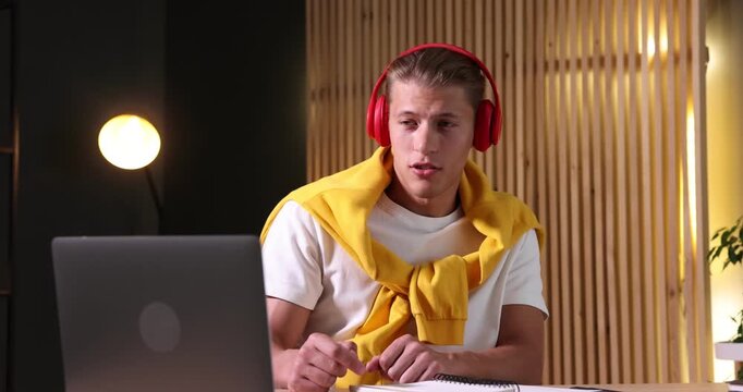 Man in headphones passing online test via laptop at table indoors