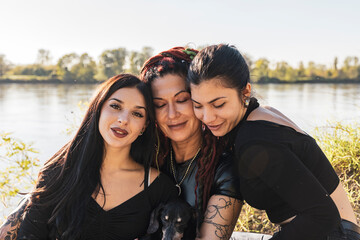 Mother embracing adult daughters and dog by river, enjoying togetherness and family love