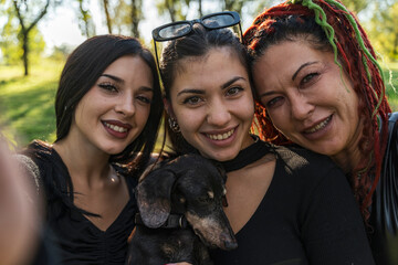 Three smiling women and dog enjoying outdoors, capturing group selfie moment