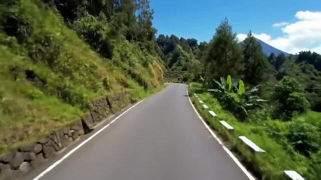 Winding road through lush green hills and mountain peaks under bright blue sky