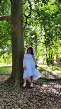 A girl in a white dress and a veil, the image of a scary bride, moves like a zombie on the street, in the park on Halloween
