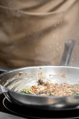 Close-up of hot food cooking in a frying pan with steam rising, mushrooms and herbs sautéed, hand sprinkling seasoning, kitchen scene with shallow depth of field.