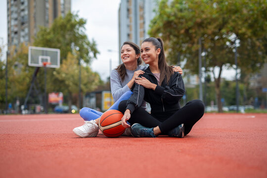 Young women friends resting on basketball court together