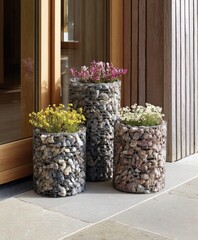 Three stylish cylindrical planters, filled with various stones and plants, are arranged attractively on a light gray patio.