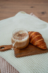 Cup of hot latte with foam, candle, knitted blanket. Home cozy decor.