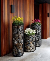 Three tall planters, filled with stones and vibrant flowers, adorn a modern wooden exterior wall.