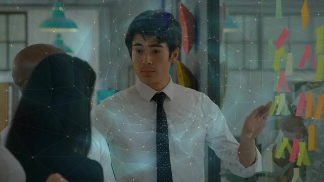 Business team gathering sparking man wearing tie laying out ideas using sticky notes on glass board