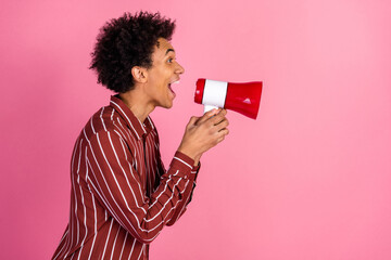 Young man enthusiastically using red megaphone against pink background promoting ideas with vibrant...