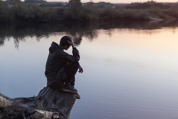 A lonely young man sits on the river bank on a cold autumn evening