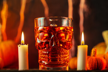Red Halloween cocktail in a skull glass on a table by candlelight