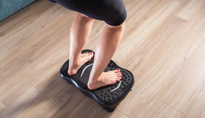 Women's legs stand on a sports vibration platform at home. Concept of doing sports at home. Modern home exercise machine, close-up