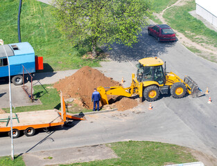 A yellow excavator dug up a road to lay electrical cables, workers stand near the hole, industry. Copy space for text