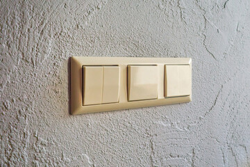 Triple beige light switch mounted on a textured wall indoors. Electrical switch panel for controlling lighting.