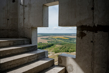 A cross-shaped window made of stone with a view of the summer landscape