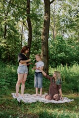 Obraz premium A young mother joyfully plays with her daughter and son in nature, sharing authentic family moments of laughter and connection. Pure love and outdoor happiness