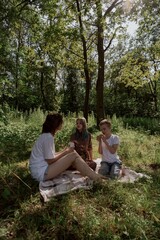 Fototapeta premium A young mother joyfully plays with her daughter and son in nature, sharing authentic family moments of laughter and connection. Pure love and outdoor happiness