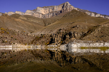 Panorama of autumn mountains with terracotta slopes and a clear lake