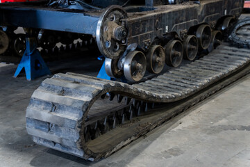 Heavy-duty crawler machine undergoing repair with loose rubber track beside wheels and rollers,...