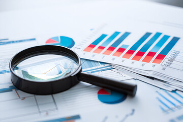 Fototapeta premium Analyzing business data: a magnifying glass sits on charts and graphs, symbolizing careful review and insight.