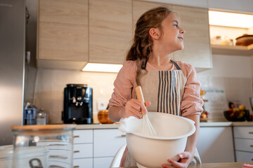 Little cute girl is beating eggs in the kitchen. Homemade baking. Cozy autumn.