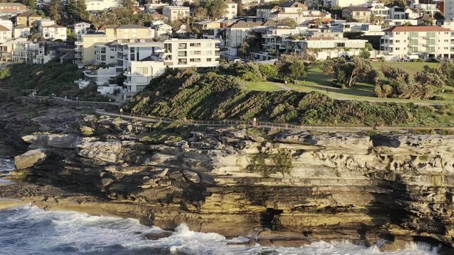 Drone video near Mackenzie's point lookout just South of Bondi Beach showing runners and walkers on the coastal track during sunrise. Shot reveals more of the Southern side toward Tamarama