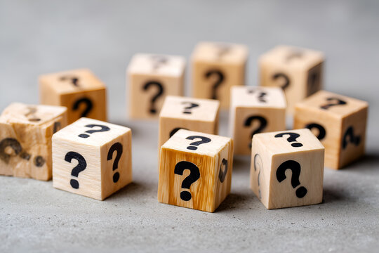 Wooden cubes are scattered across a gray surface, each adorned with a question mark, symbolizing uncertainty and inquiry.