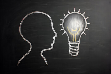 Head profile and lightbulb drawn in white chalk on a blackboard background symbolizing innovation, ideas, and creative thinking.