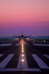 Airplane approaching a runway at dusk. The aircraft is centered, illuminated by runway lights under a beautiful sky.