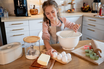 Little cute girl is beating eggs in the kitchen. Homemade baking. Cozy autumn.