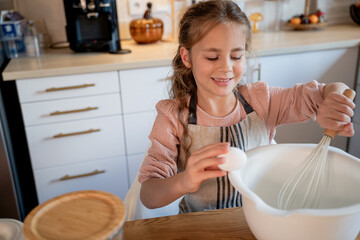 Little cute girl is beating eggs in the kitchen. Homemade baking. Cozy autumn.