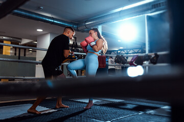 Female kickboxer training in boxing ring with male trainer at gym.